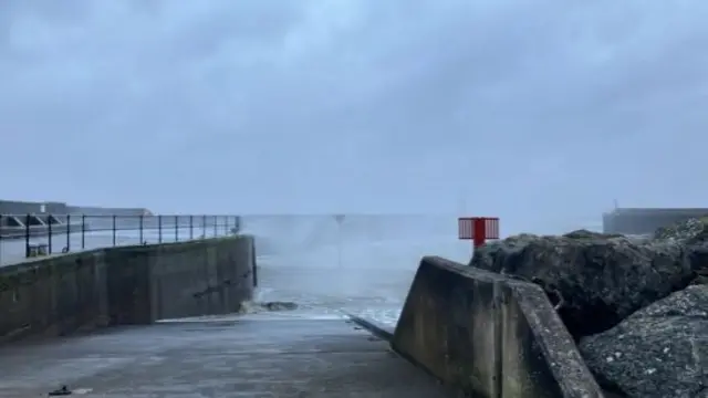 View of seaside walk during Storm Darragh. Sky is cloudy and the wind is pushing up waves and water