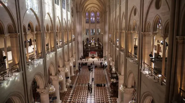 Wide shot of inside Notre-Dame cathedral as guests start to arrive. Rows of chairs take up most of the nave