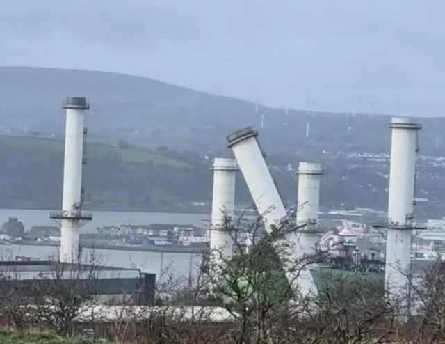 Five white power plant chimneys, one of them is leaning to one side