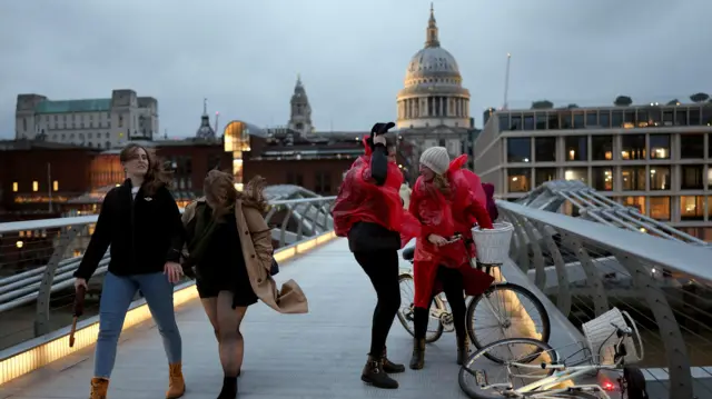 A woman walks during a gust of wind on Millennium Bridge after Storm Darragh hit the country, in London