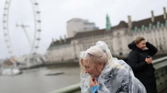 A tourist wearing a raincoat walks on Westminster Bridge during a gust of wind, after Storm Darragh hit the country, in London,