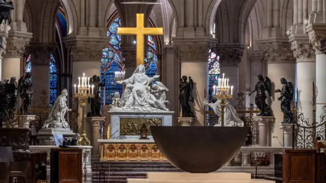 The statues from the Vow of Louis XIII. The statues are large and white, two depicting men and one depicting a woman. A large golden Christian cross is at the back of the room in front of blue-stained glass windows.