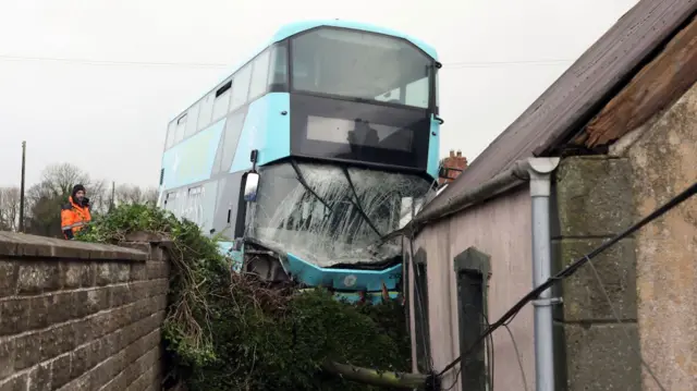 A damaged blue double decker bus crashed into the side of an old building