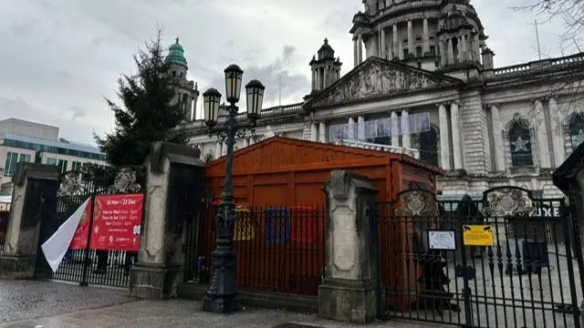 Belfast City Hall with the gates closed. Christmas market stalls and a Christmas tree can be seen within the grounds.