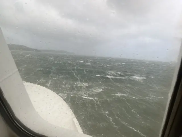 Stormy sea seen through a window covered in rain drops. A couple of headlands in the distance.