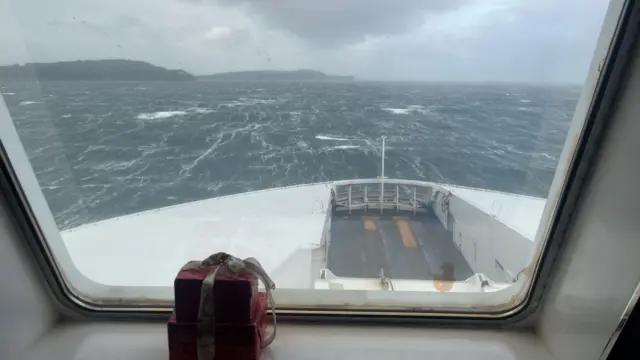 Stormy sea seen through a window covered in rain drops. A couple of headlands in the distance.