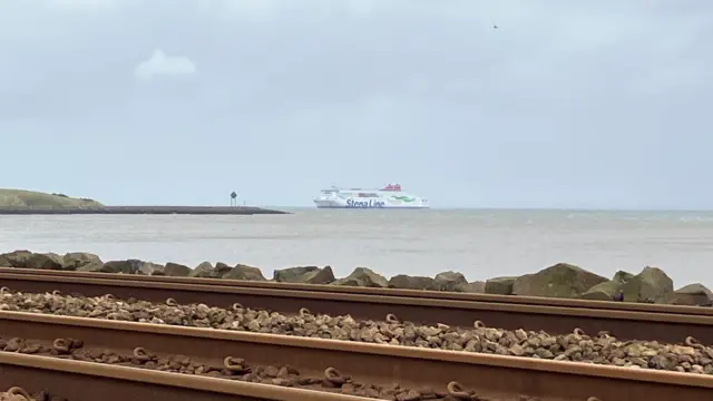 A Stena Line ferry off the coast under a cloudy sky. In the foreground some train tracks