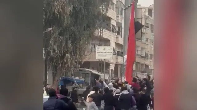 A large Syrian flag is seen being torn down by people