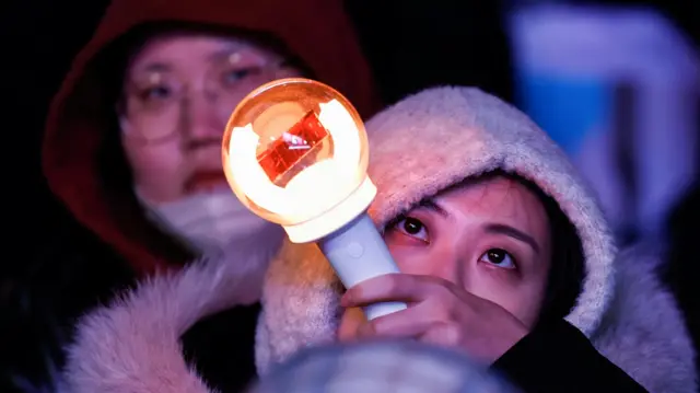 A woman holds a torch light after South Korean President Yoon Suk Yeol, who declared martial law which was reversed hours later, survived an impeachment motion, at a rally in front of the National Assembly in Seoul, South Korea