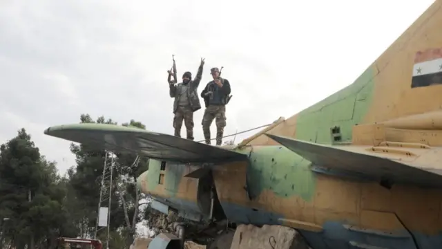 A rebel fighter gestures the victory sign while standing on a military aircraft that belonged to forces loyal to Bashar al-Assad government, inside Hama's military airpor