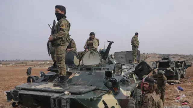 Group of soldiers standing on tank, looking out to the countryside around them