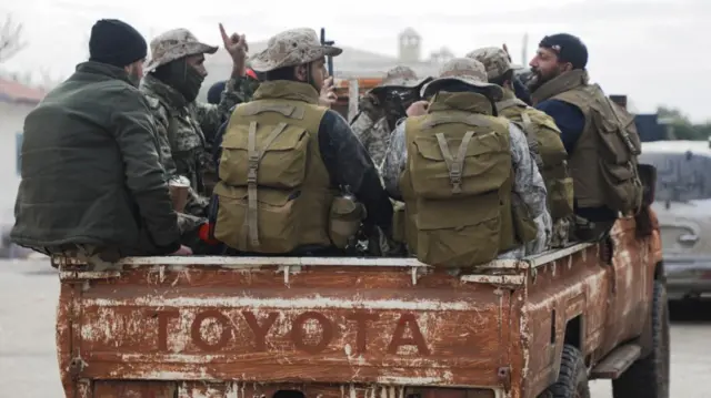 Group of men on the back of a Toyota van driving through the countryside outside Homs