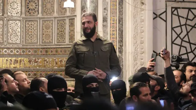 Abu Mohammad al-Jawlini stands addressing a crowd below him