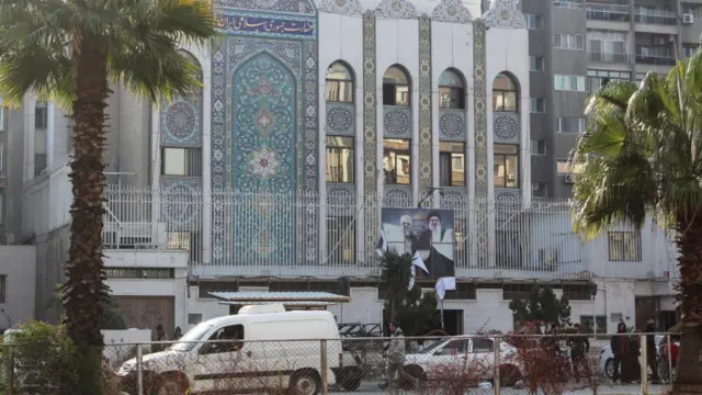 The front of the Iranian embassy in Damascus. A large image on the front of the building is clearly torn, and a at least one window is smashed, but the scene appears calm and there is little sign of a crowd