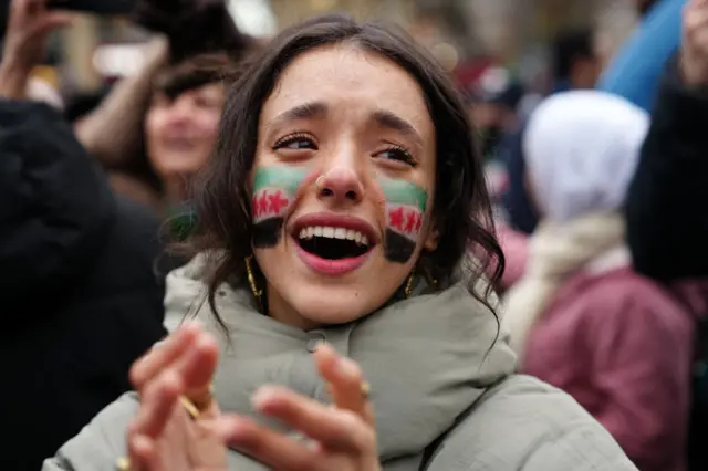 A woman, with an opposition flag painted on her face, applauds as members of the Syrian community and supporters gather to celebrate the fall of Syrian president Bashar al-Assad in the face of an offensive by Islamist-led rebels, in Paris