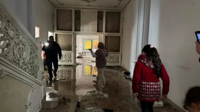 People walk through a dark hallway next to ornate stairs