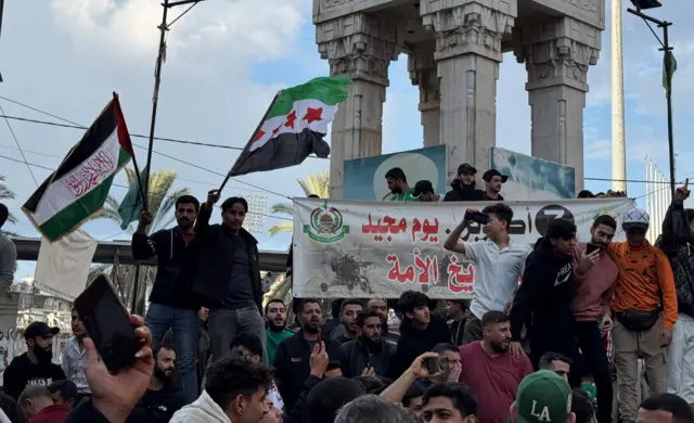 A group of men stand together, with some waving Syrian rebel flags