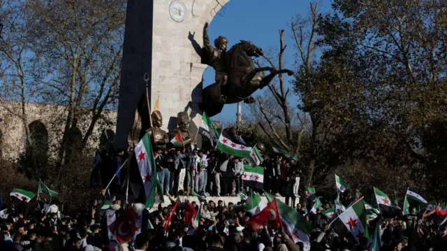 A large crowd gathers, waving Syrian opposition flags