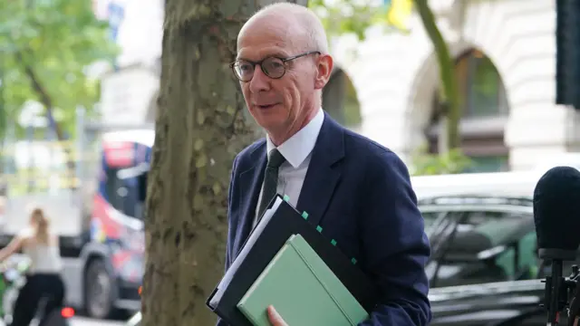 Pat McFadden waling in the street carrying a green folder.