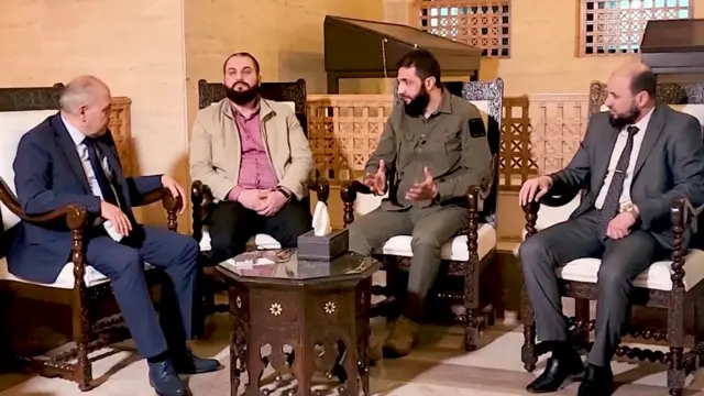 al-Jolani meeting with the prime minister and two other men - all four are sitting in chairs and talking