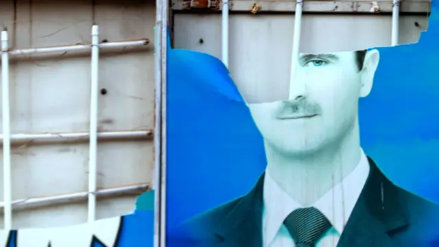 A damaged portrait of Syrian President Bashar al-Assad is hangs