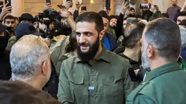 Abu Mohammed al-Jawlani at the Umayyad Mosque in Damascus with dozens of his supporters behind him trying to take his photo.