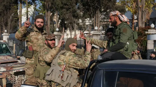 Rebel fighters in a camouflage uniform sit in a truck making gestures with their hands