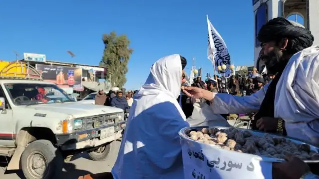 Taliban fighters hand out sweets to people in the streets of Afghanistan