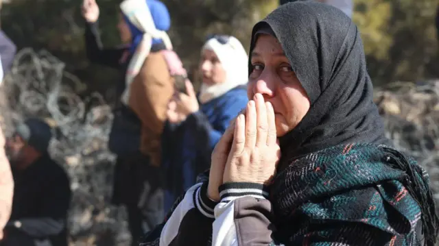 A woman holds her hands together and looks at the camera by a crowd outside the prison