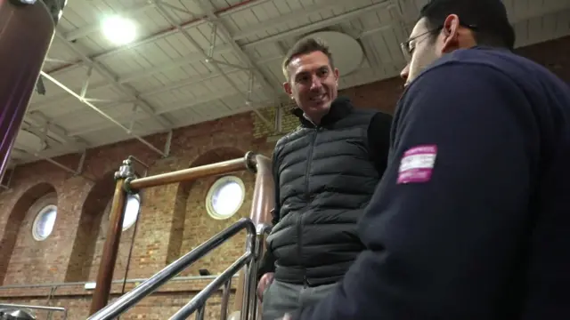 A BBC producer talking to Stephen Russell in his distillery. The angle is tilted upwards and they are speaking to each other