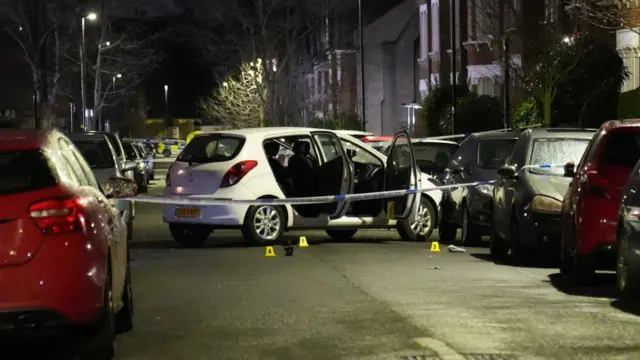 A white hatchback car stands abandoned in a London street