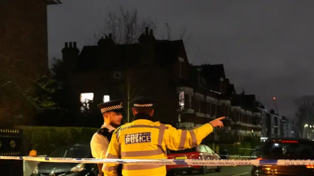 A police officer, wearing a bright yellow coat, points while taking to another uniformed officer