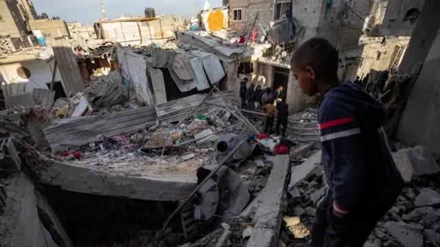 A child looks on as Palestinians inspect a destroyed area following an Israeli airstrike on the Rafah refugee camp, southern Gaza Strip, 12 February 2024.