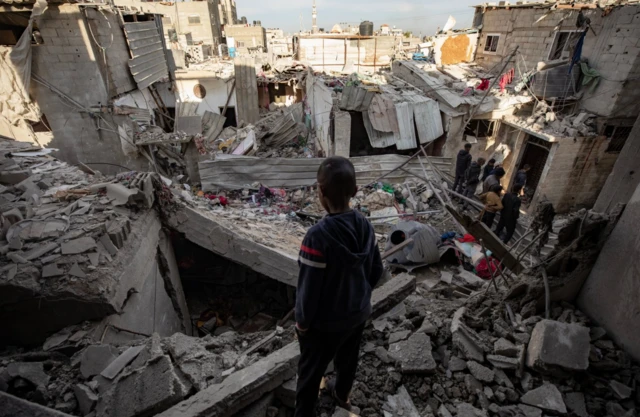 A child looks on as Palestinians inspect a destroyed area following an Israeli airstrike on the Rafah refugee camp