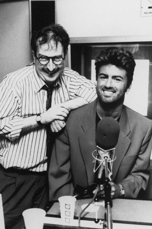 A black and white image of Steve Wright standing next to a seated George Michael in a radio studio