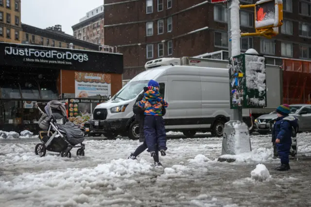 A woman carries a child over a large puddle as a large winter storm makes its way across the area on February 13, 2024 in New York City