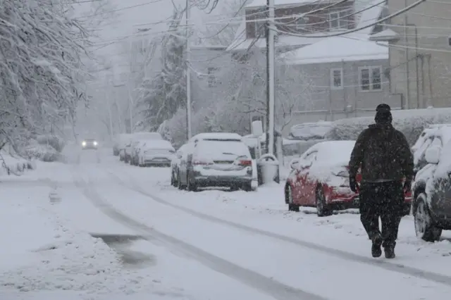 A man walks on a snow covered road during a snowfall at Hudson County in New Jersey, United States on February 13, 2024