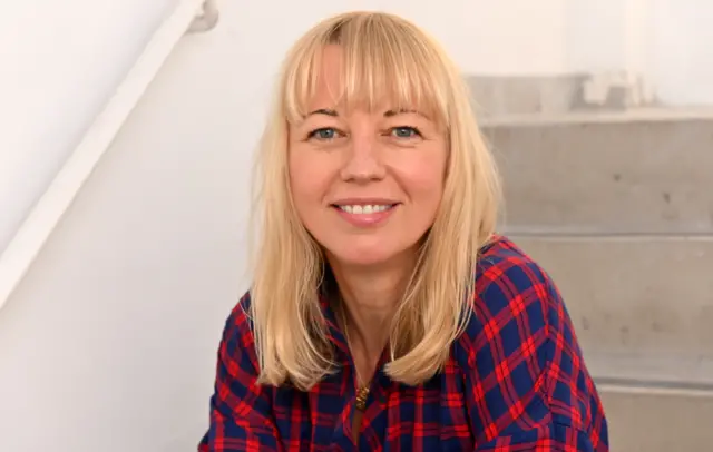 Sara Cox looks directly at the camera with a blue and red chequered shirt on