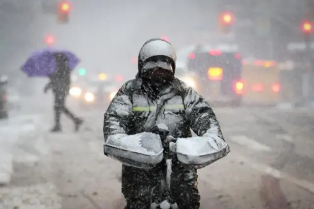 A snow-covered delivery worker is seen in New York City on Tuesday morning