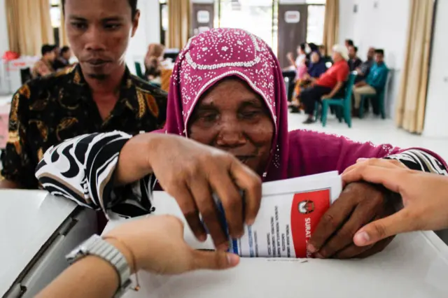 A blind woman is helped to cast her ballot at a polling station in Medan