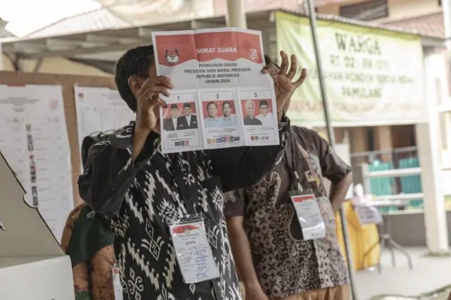 Election workers hold up ballots against light while counting