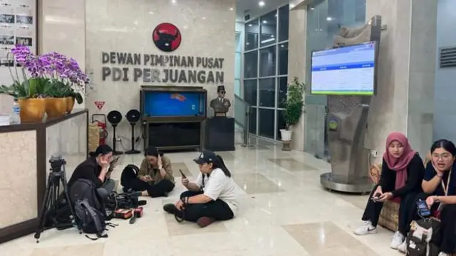 A few people with cameras sit on the floor with 'PDIP Leadership Council' written on the wall behind them