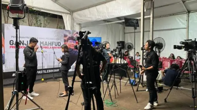 Camera crews at an otherwise almost empty stage area in front of a Ganjar-Mahfud billboard