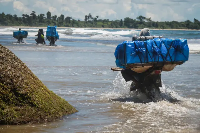 Election workers ride motorbikes on the beach to deliver election materials