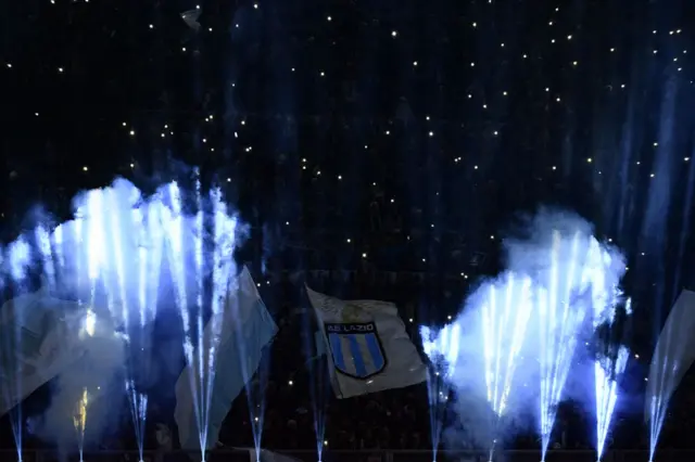 Lazio fans wave flags and set off flares as the teams enter the pitch.