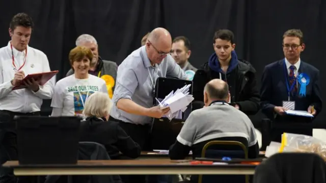 Ballot boxes arrive at the Wellingborough by-election at the Kettering Leisure Village, Northamptonshire. A man is seen empty a box of papers onto a table