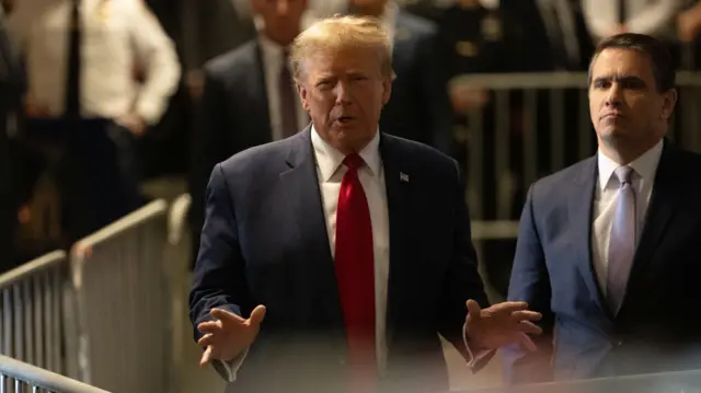 Donald Trump standing behind a metal barricade and gesturing with his hands