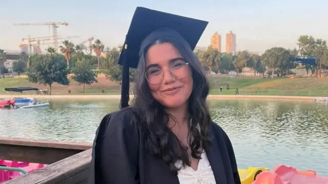 Noa Marciano wearing a mortar board and gown next to a body of water