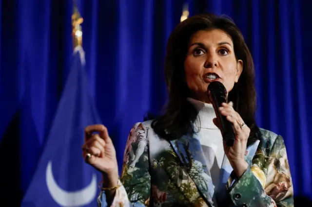 Nikki Haley wearing a green and white patterned and speaking into a mic at a campaign rally in South Caroline