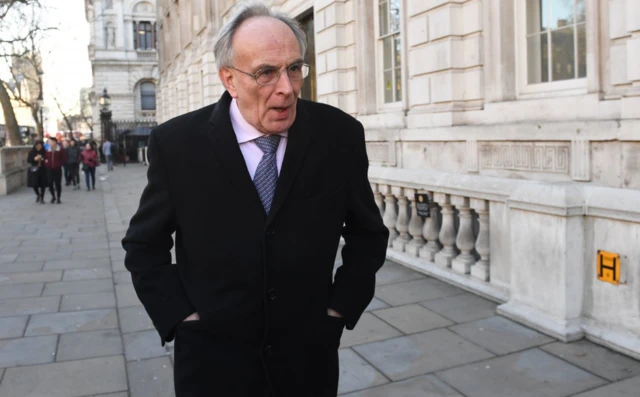 Peter Bone walks with his hands in his pockets along a street in Whitehall, London